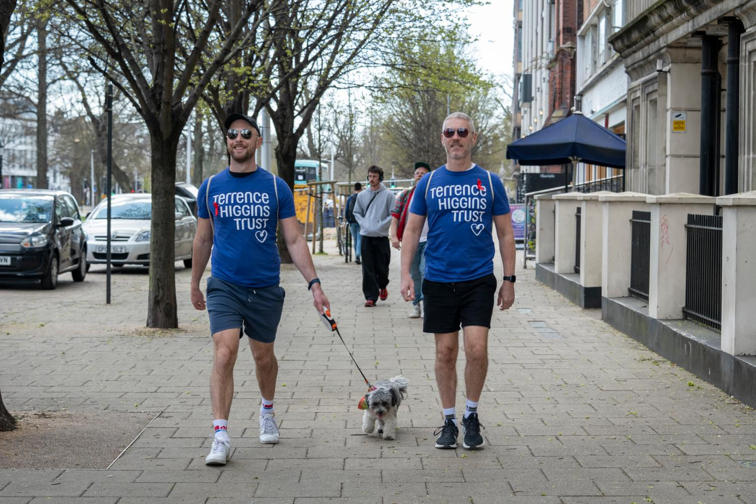 Two men in Terrence Higgins Trust t-shirts with a dog on a leash.