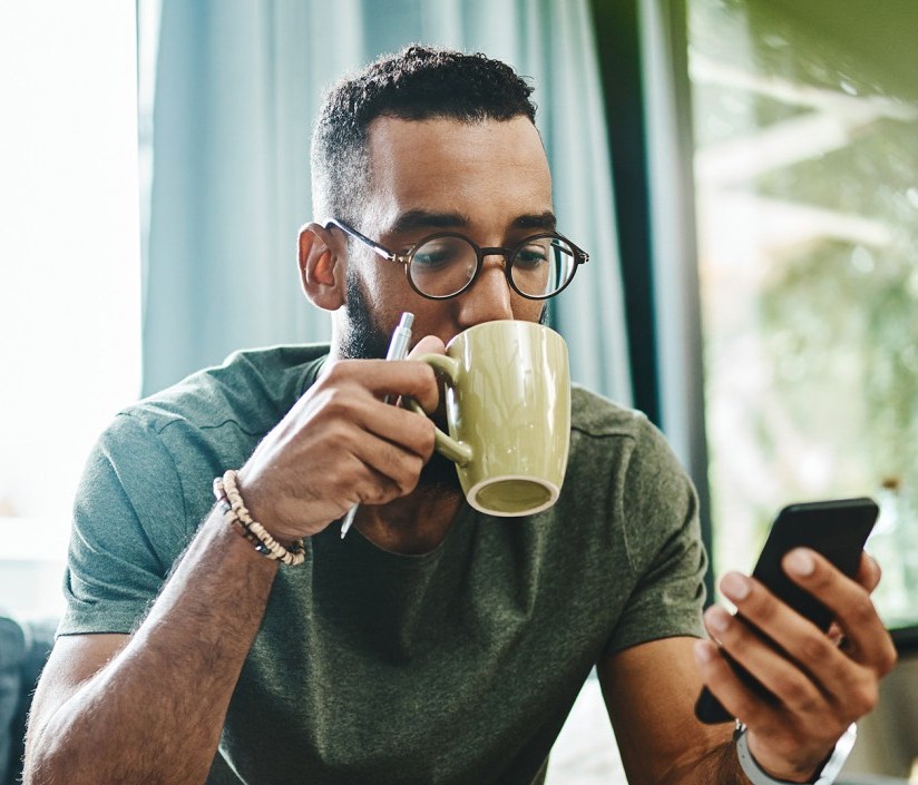 A person drinks from a mug while looking at their phone.