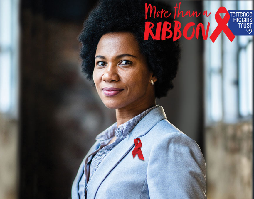 A woman looking towards the camera with a red ribbon on her lapel.