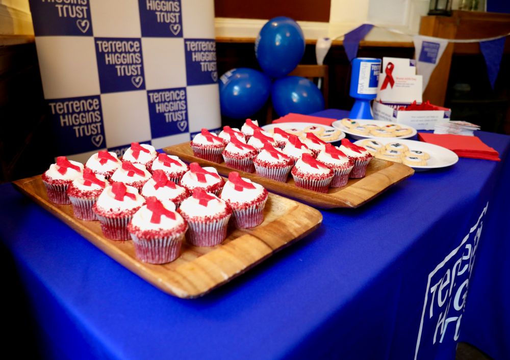 Cupcakes in a bake sale on a blue Terrence Higgins Trust tablecloth.