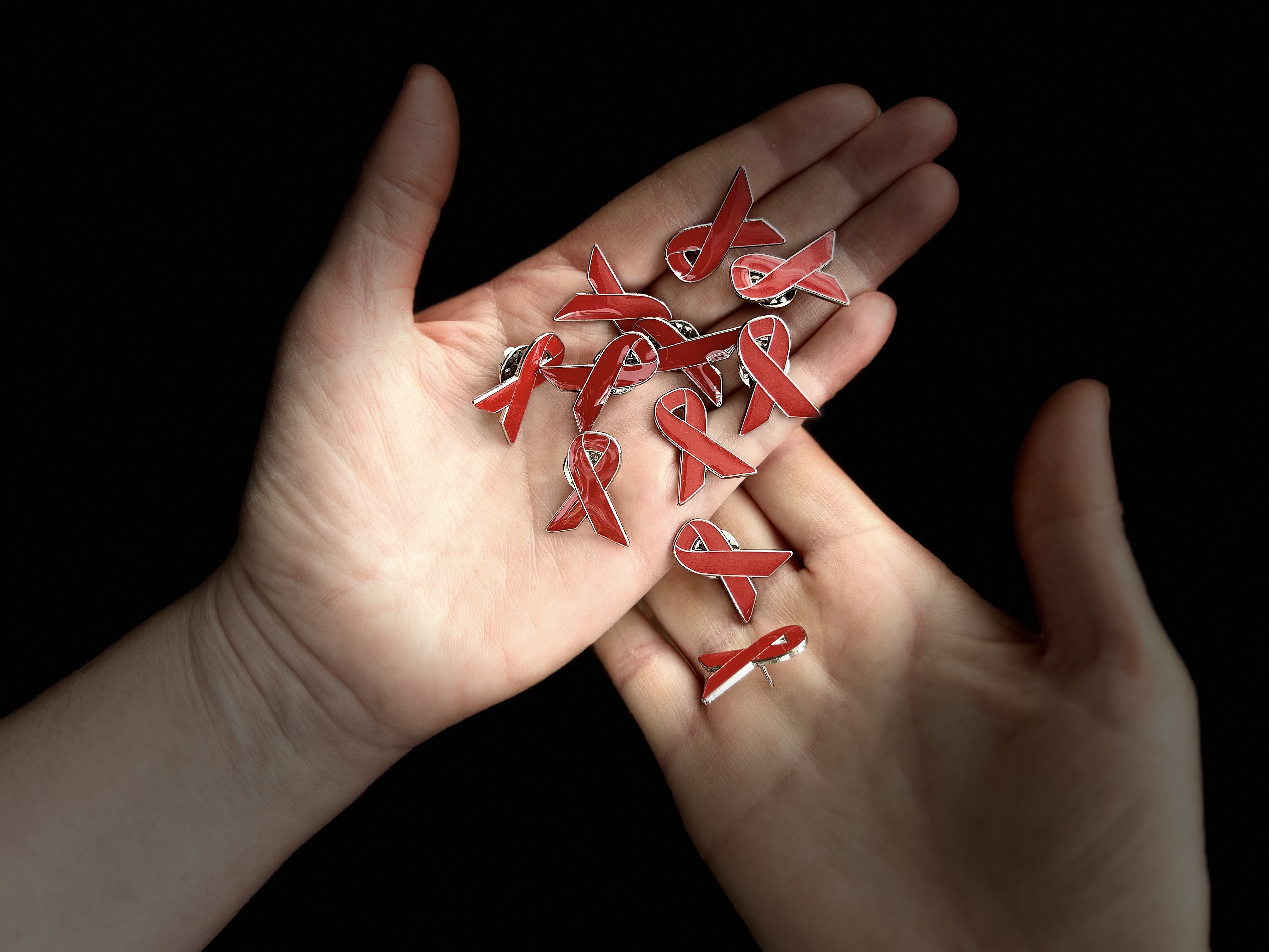 Enamel pin badges of red ribbons in a pair of hands.