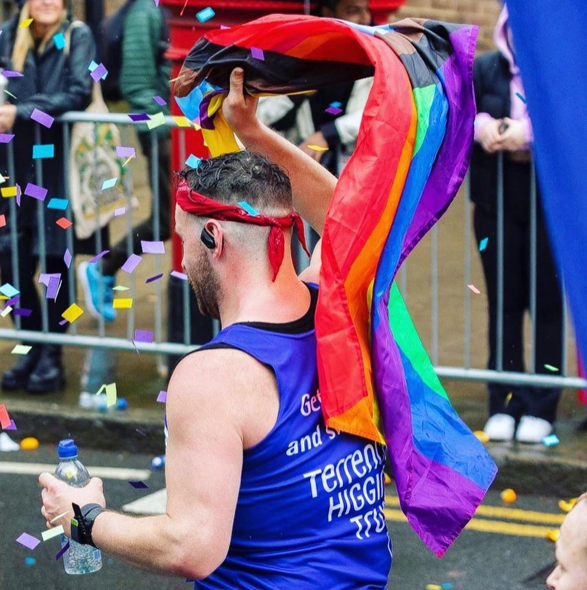 Side shot of a Terrence Higgins Trust marathon runner with the Pride flag in view.