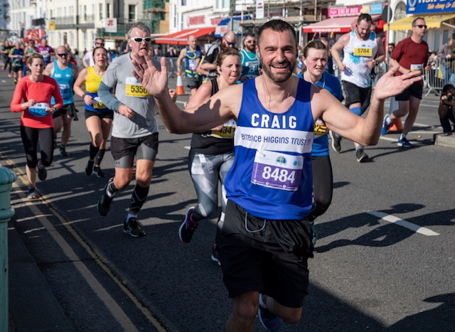 A smiling and waving Terrence Higgins Trust marathon runner.