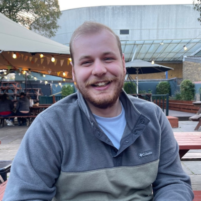 A man is sitting outside, smiling at the camera.