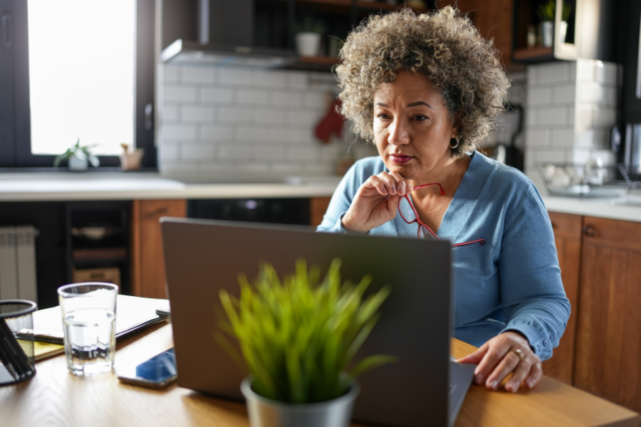 An older woman works at a laptop at a kitchen table.