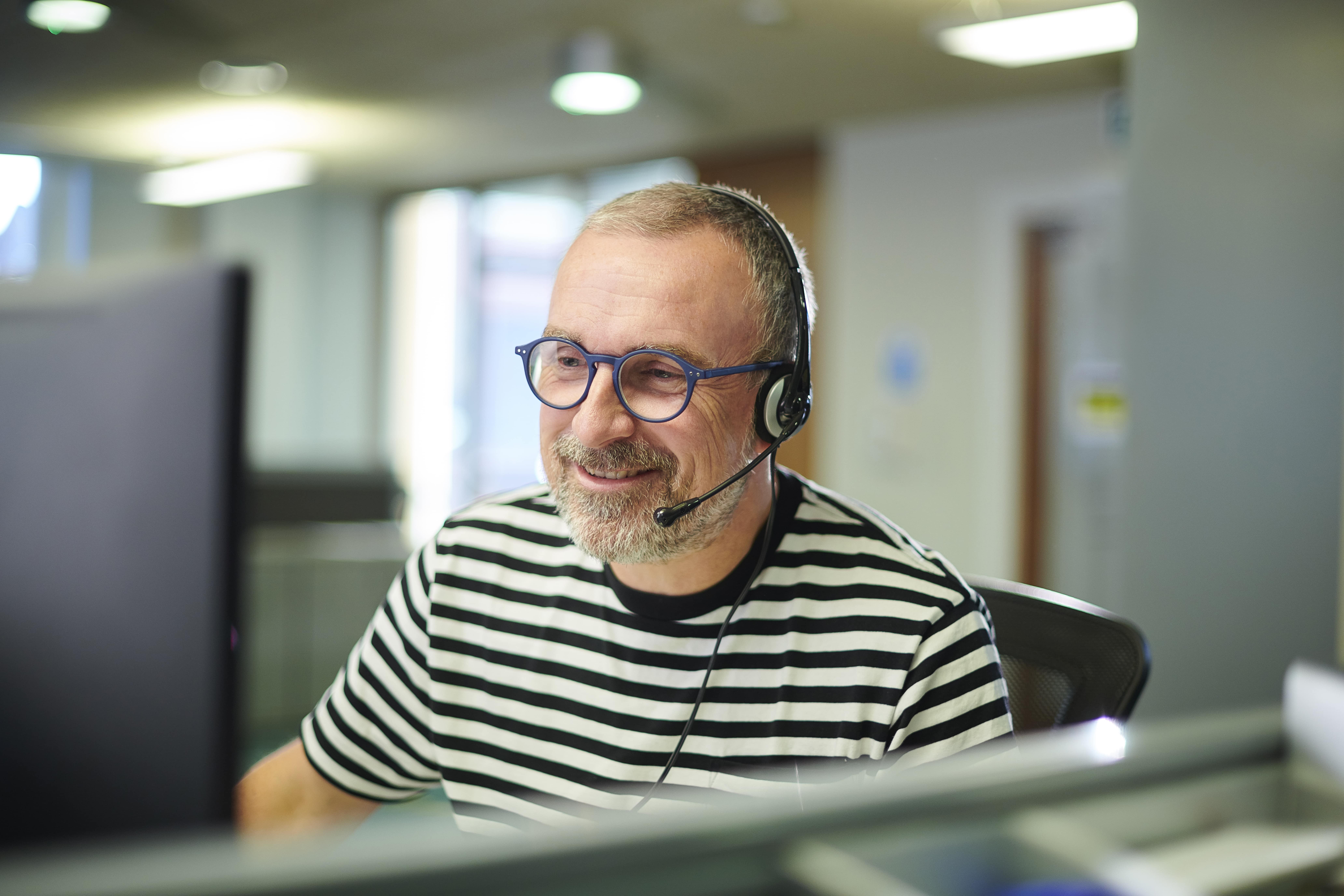 A person in a striped tshirt in front of a computer with a headset on.