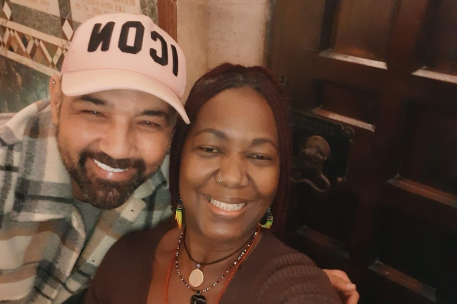 Two friends embracing. The man has his arm around the woman and they are smiling at the camera.