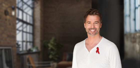 A smiling white man in a white shirt with red ribbon pinned to it. 