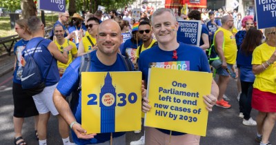 Richard holds up a 2030 placard square and Eugene is holding up a Terrence Higgins Trust rainbow logo placard.