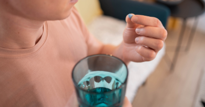 Person holding a blue pill in their hand and a glass of water.