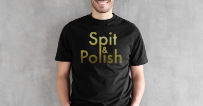 A model against a grey background wearing a black T-shirt with gold 'Spit & Polish' slogan.
