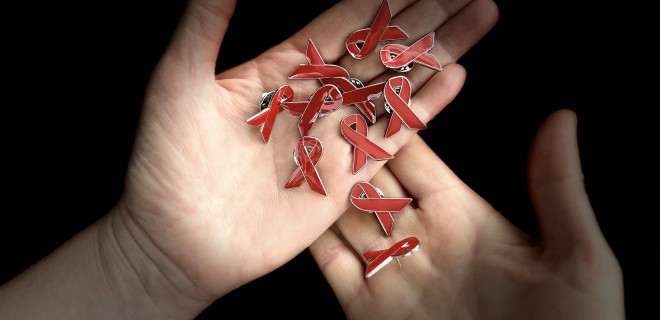 Enamel pin badges of red ribbons in a pair of hands.