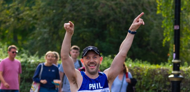 A Terrence Higgins Trust marathon runner with his arms up in jubilation.