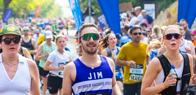 A Terrence Higgins Trust runner with sunglasses, holding a water bottle at the London Marathon.