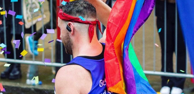 The back of a Terrence Higgins Trust marathon runner with the pride flag in the background.