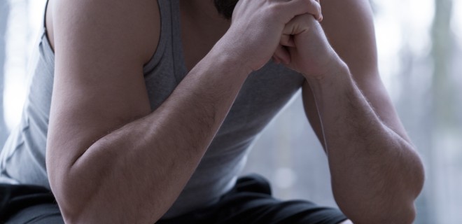 A man sitting with and hands towards his face with a sad facial expression.