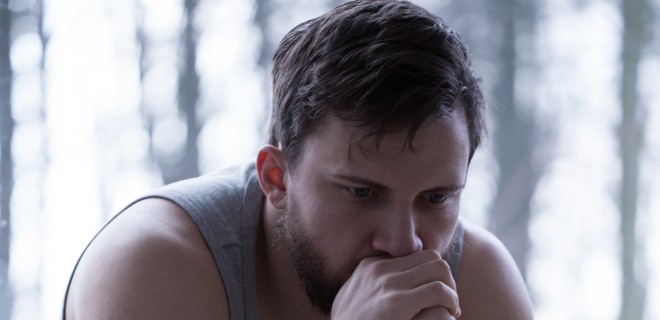 A man sitting with and hands towards his face with a sad facial expression.