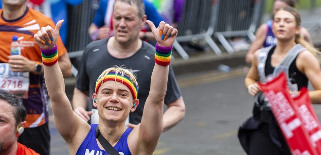 A smiling Terrence Higgins Trust marathon runner with both arms up.