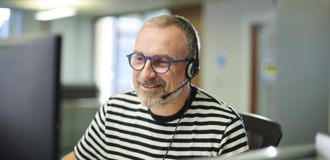 A person in a striped tshirt in front of a computer with a headset on.