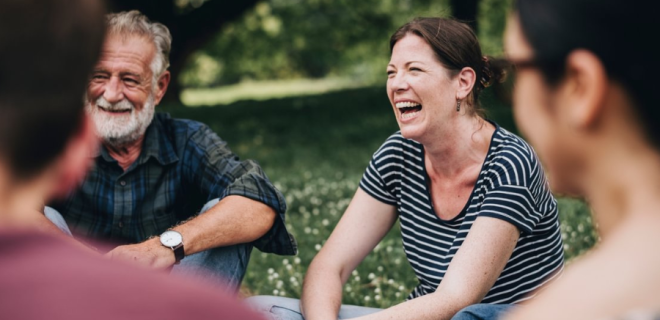 A group of people sitting in a circle in a park, smiling and laughing.
