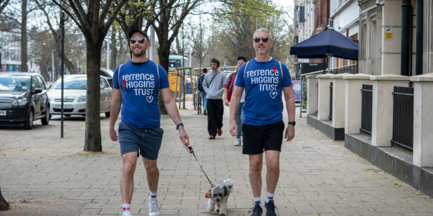 Two men in Terrence Higgins Trust t-shirts with a dog on a leash.
