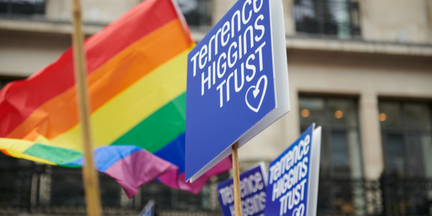 Terrence Higgins Trust logo placards and Pride flags at a Pride march.