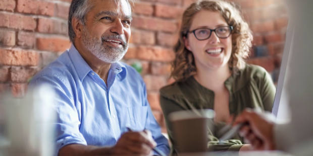A couple sit together at a table talking to another person.