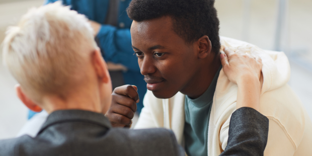 A person is being comforted by someone else, with their hand on their shoulder.