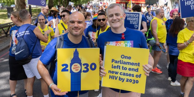Richard holds up a 2030 placard square and Eugene is holding up a Terrence Higgins Trust rainbow logo placard.