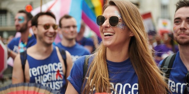 A group of people at a Pride march. They're wearing Terrence Higgins Trust blue t-shirts and carrying rainbow fans.