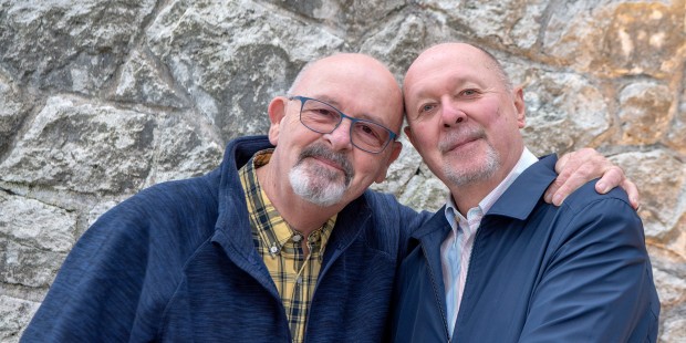 Two smiling elderly man with one's arm around the other.