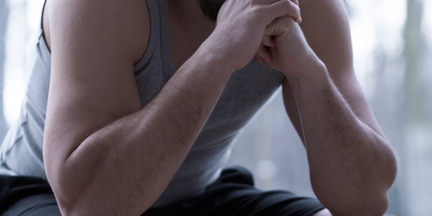 A man sitting with and hands towards his face with a sad facial expression.