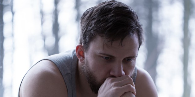 A man sitting with and hands towards his face with a sad facial expression.