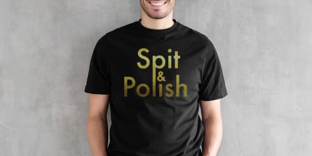 A model against a grey background wearing a black T-shirt with gold 'Spit & Polish' slogan.