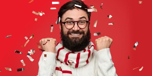 A bespectacled and smiling man with two fists up in celebration surrounded by confetti.