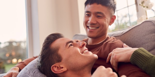 Young male couple smiling together on a sofa.