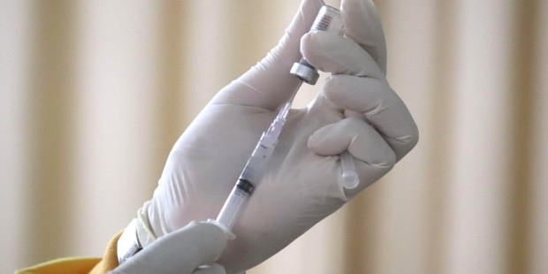 A person holds a needle and vaccine bottle in their hands.