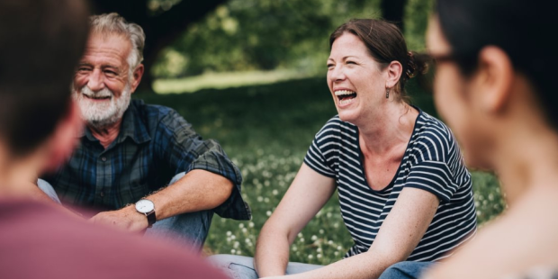 A group of people sitting in a circle in a park, smiling and laughing.