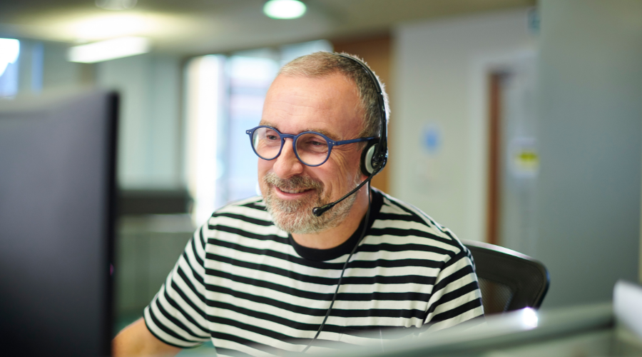 A man sits at a desk in an office, wearing a headset.
